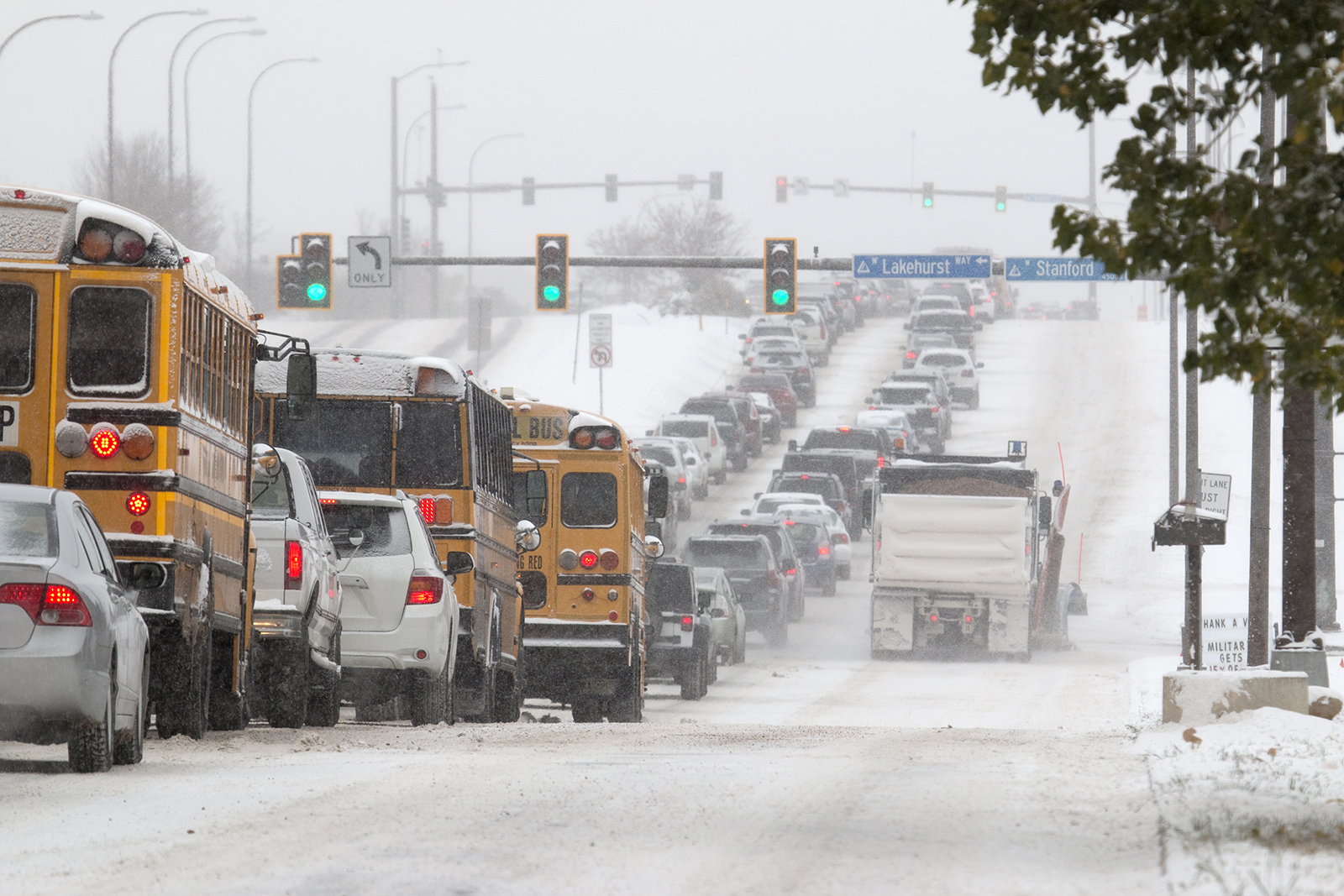 School busses and other vehicles line up on a icy and snow packed road.