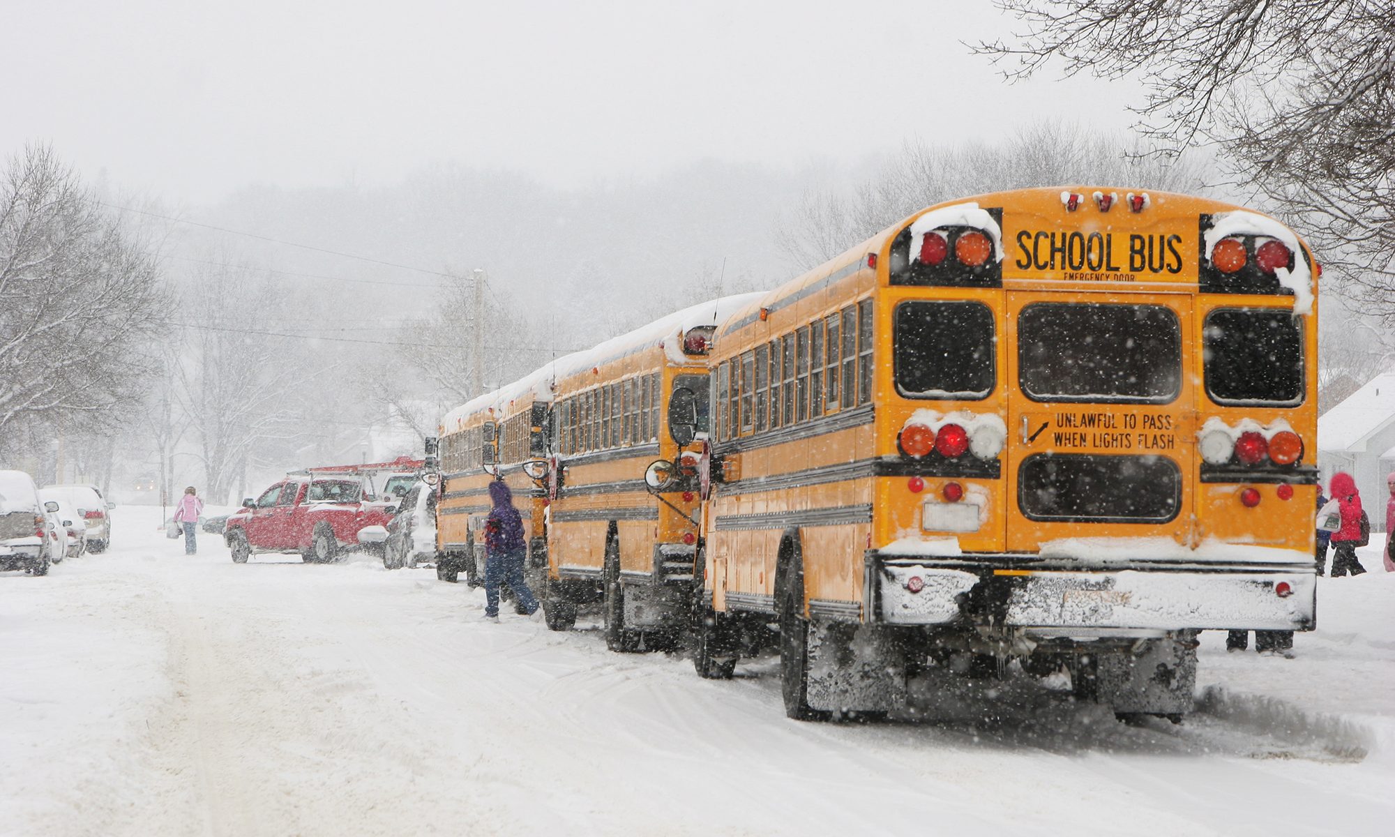 Line of buses, trucks and cars waits to pick up children getting out of school early.