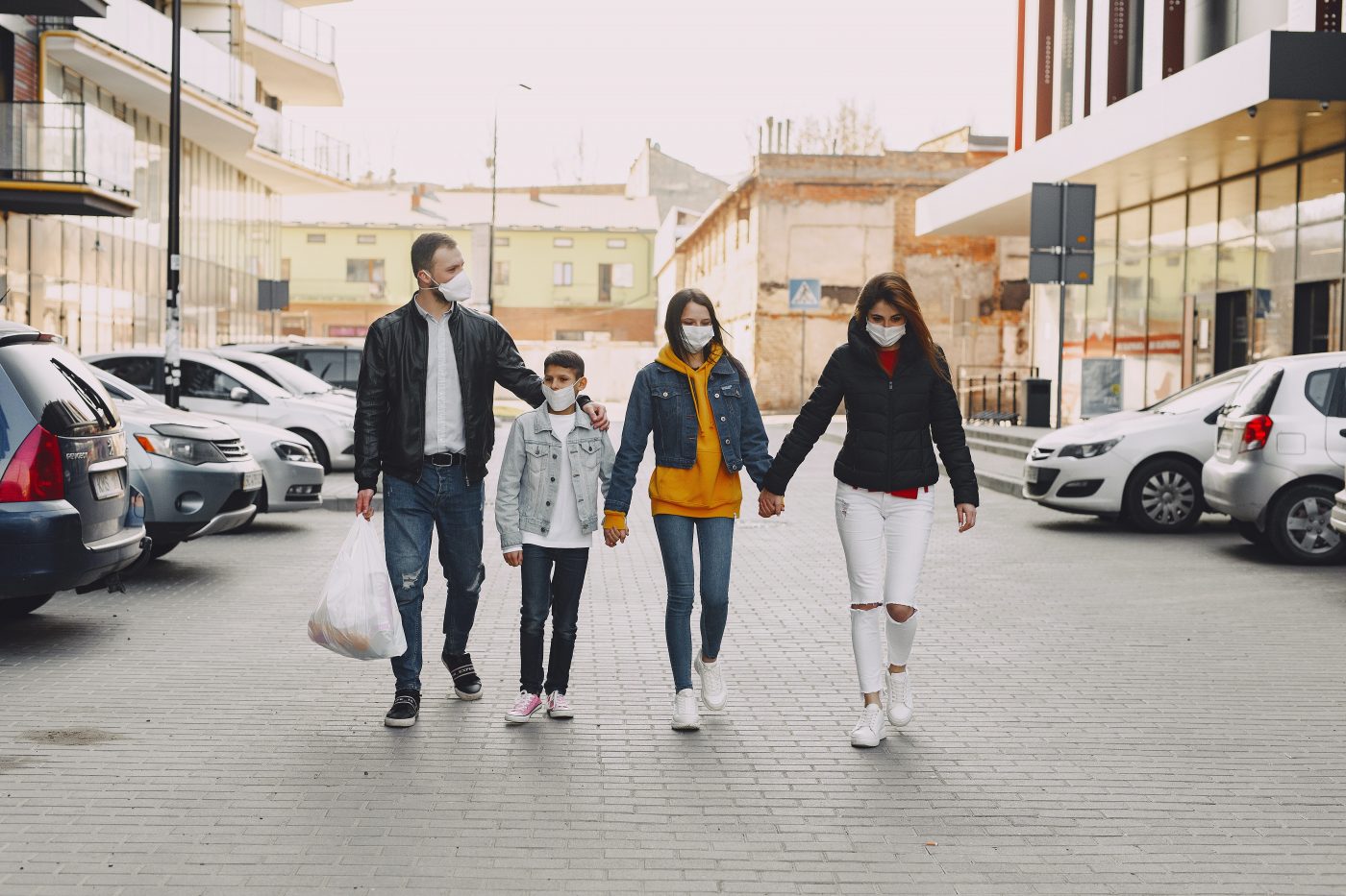 man, boy, girl, and woman walking down a street together while wearing masks