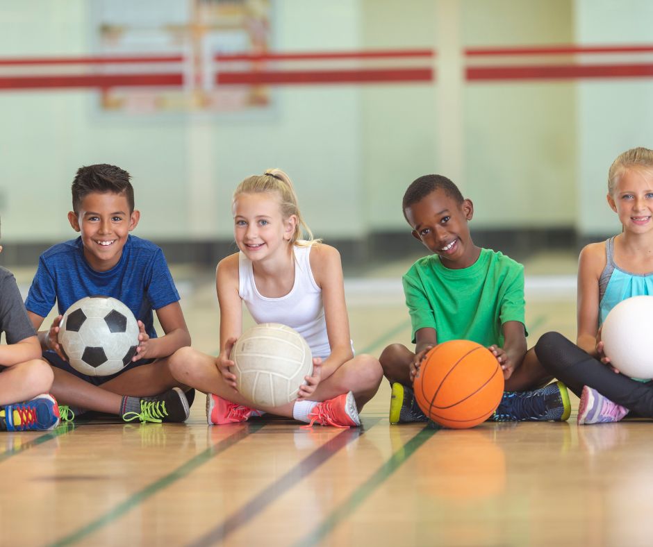 students sitting on a gym floor holding balls