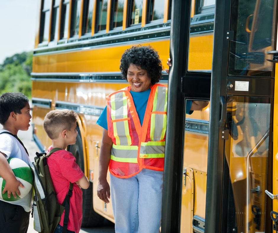 A bus attendee helping kids get on a school bus