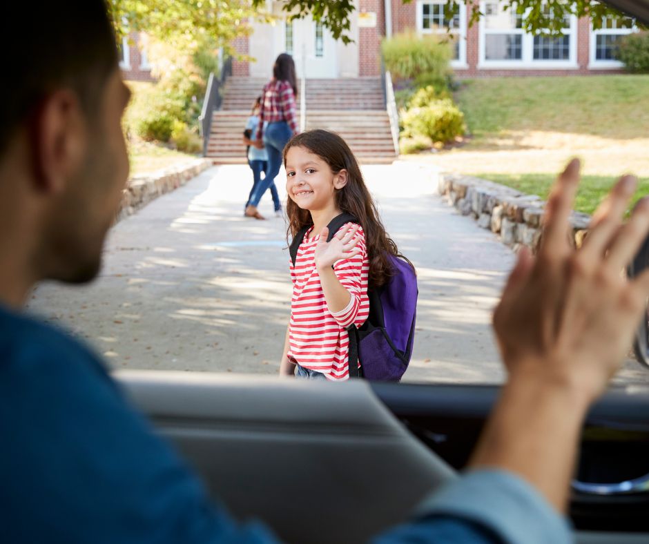 a child waving at their dad after getting dropped off in the car line at school
